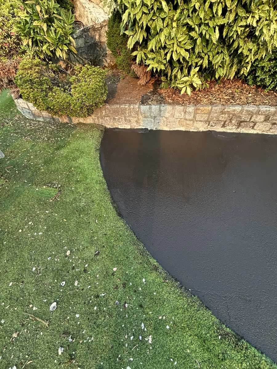 Close-up of the sealed asphalt edge cut cleanly against the lawn and stone curb